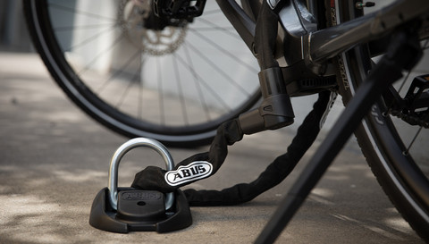 ABUS Wand-Bodenanker 100 mit einem ABUS Kettenschloss verbunden am Fahrrad gesichert ©ABUS